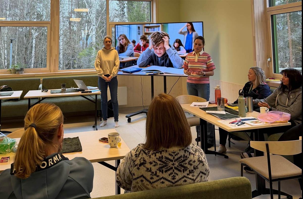 To damer som holder foredrag, tv-skjerm og lyttende mennesker - Klikk for stort bilde